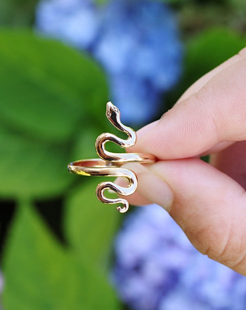 Adjustable Bronze Serpent Ring between fingers with flowers in back