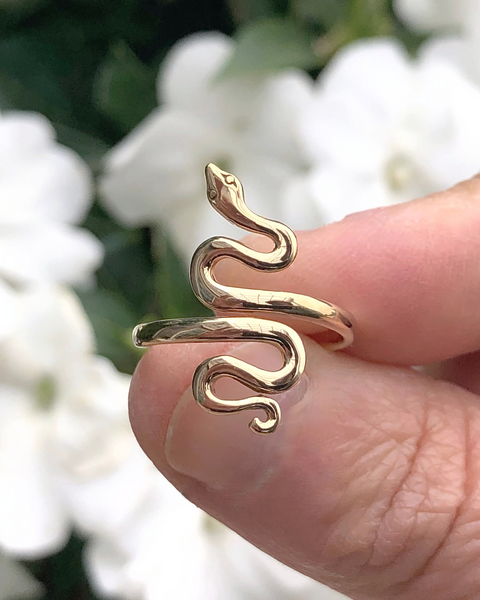Adjustable Bronze Serpent Ring between fingers with white flowers in background