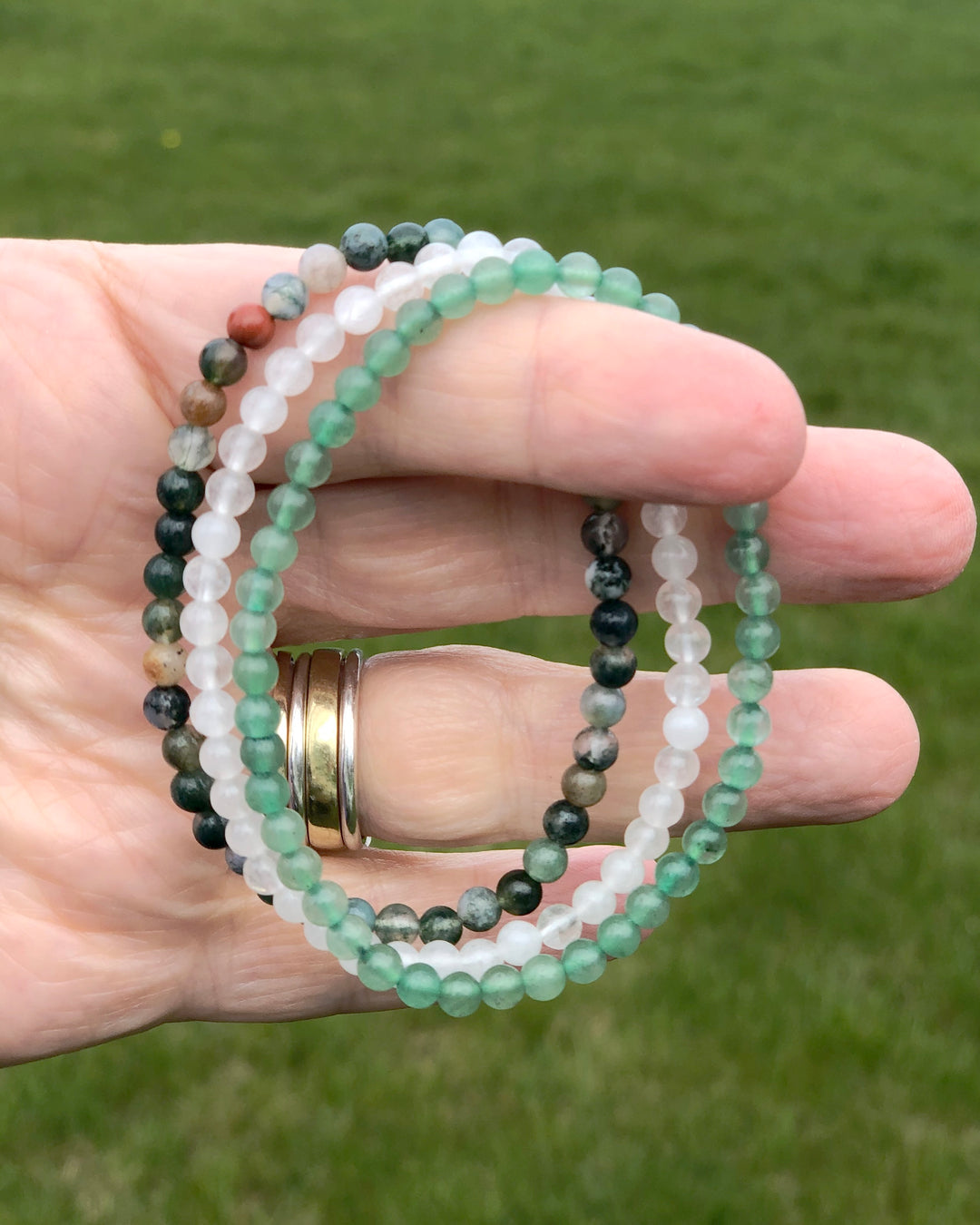 Aventurine, Snow Quartz and Indian Agate bracelets held in a hand.