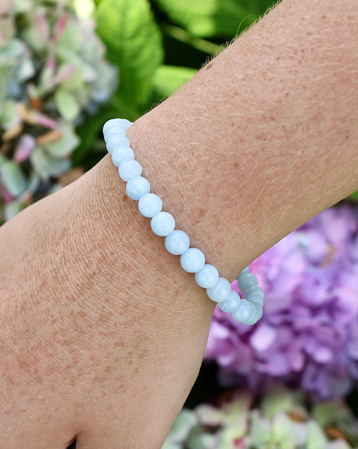 Aquamarine 6mm Beaded Gemstone Bracelet on a wrist with flowers.