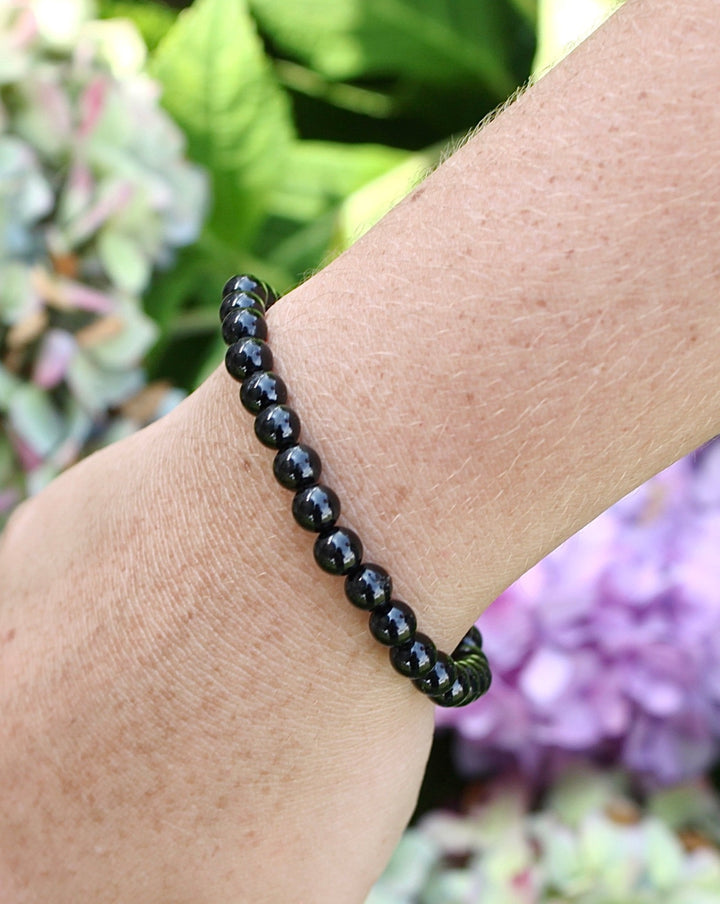 Black Tourmaline 6mm Beaded Gemstone Bracelet on a wrist with flowers.