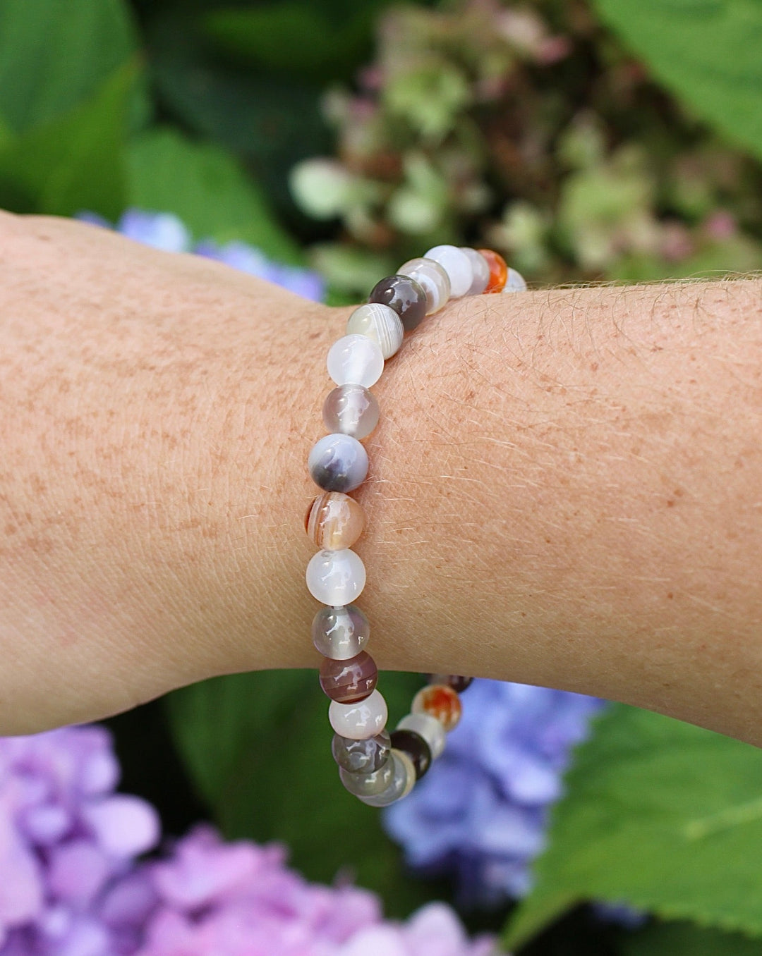 Botswana Agate 6mm Beaded Gemstone Bracelet on a wrist with flowers.