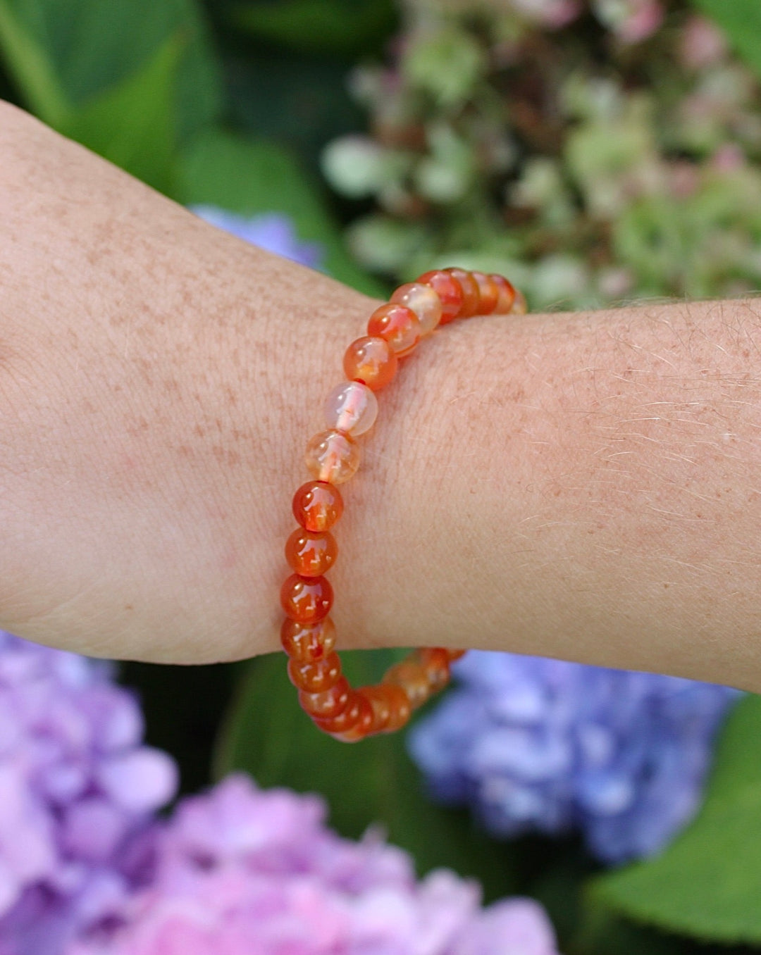 Carnelian 6mm Beaded Gemstone Bracelet on a wrist with flowers.