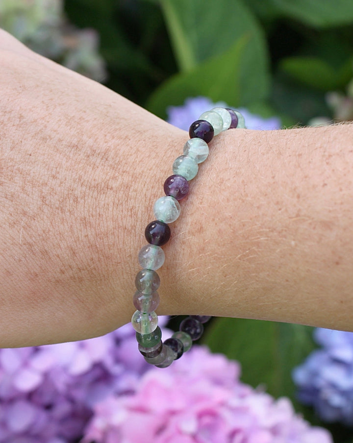 Fluorite 6mm Beaded Gemstone Bracelet on a wrist with flowers.