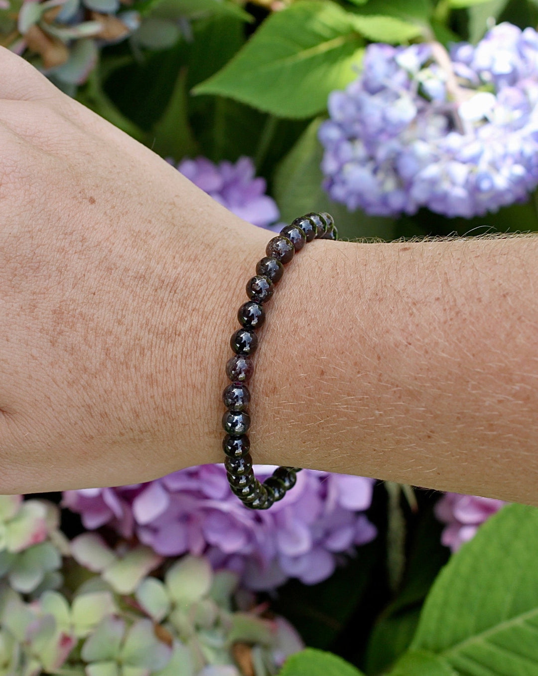 Garnet 6mm Beaded Gemstone Bracelet on a wrist with flowers