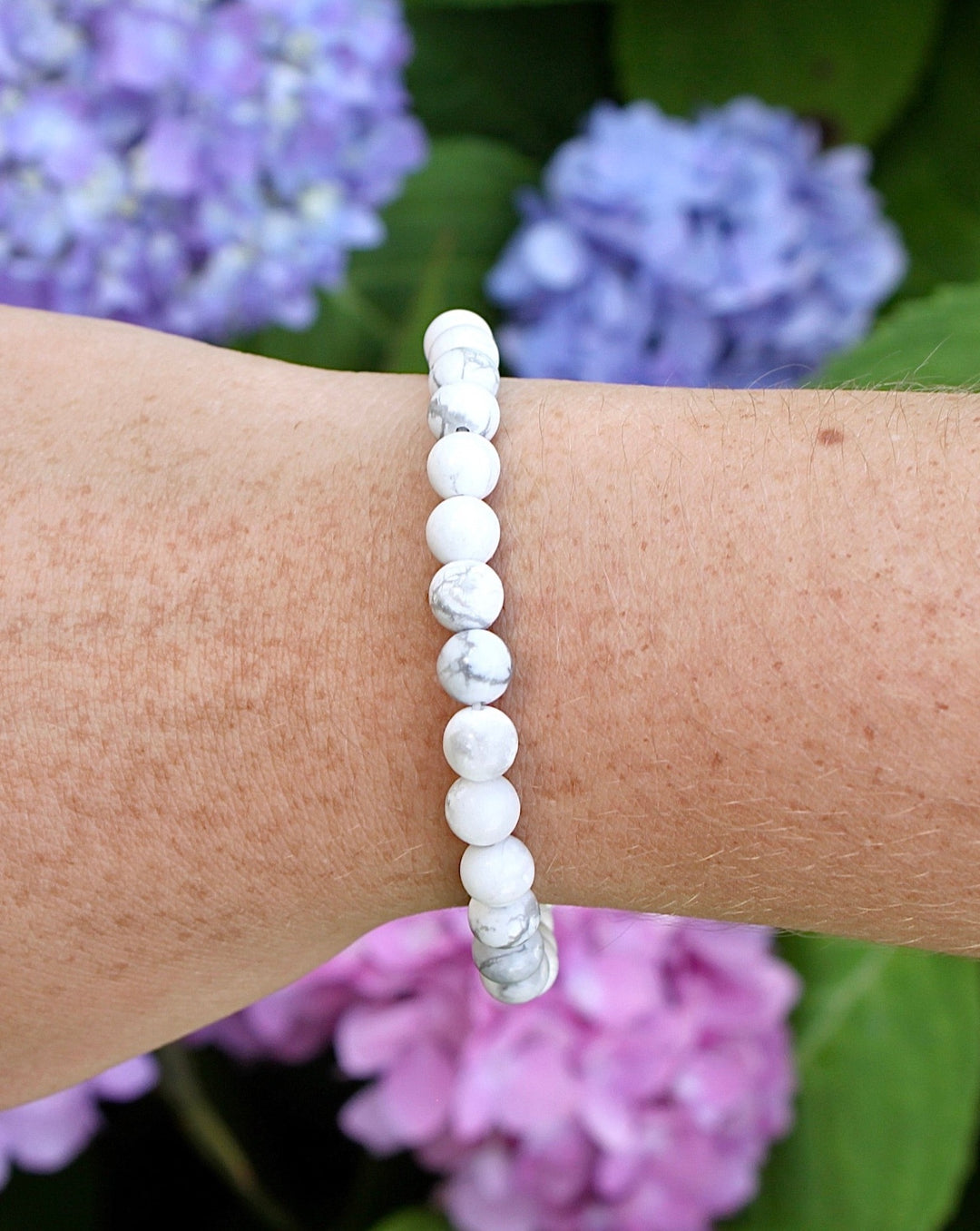 Howlite 6mm Beaded Gemstone Bracelet on a wrist with flowers.