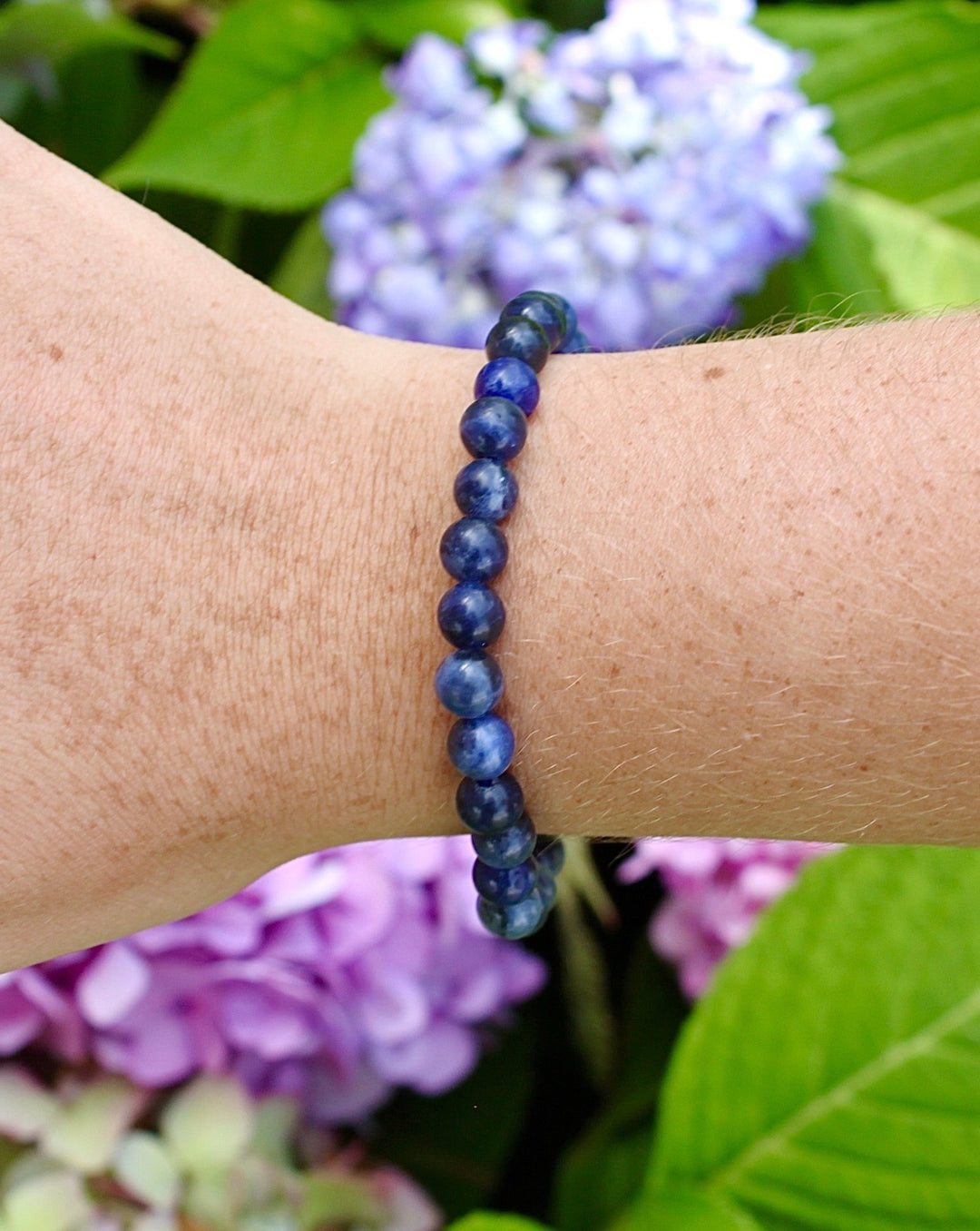 Lapis Lazuli 6mm Beaded Gemstone Bracelet on a wrist with flowers.