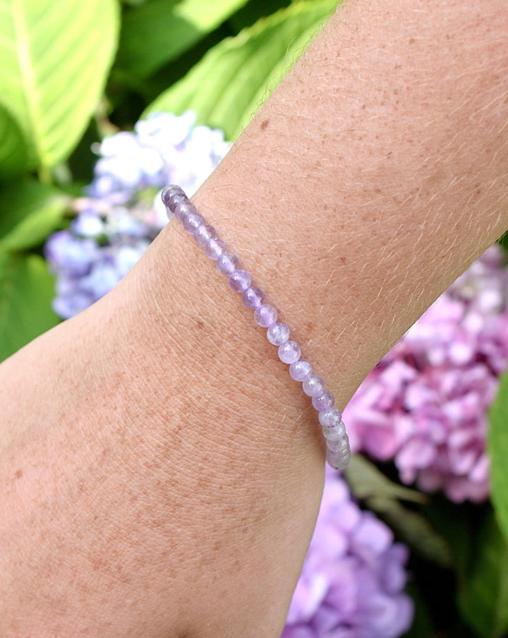 Lavender Amethyst 4mm Beaded Gemstone Bracelet on a wrist with flowers.