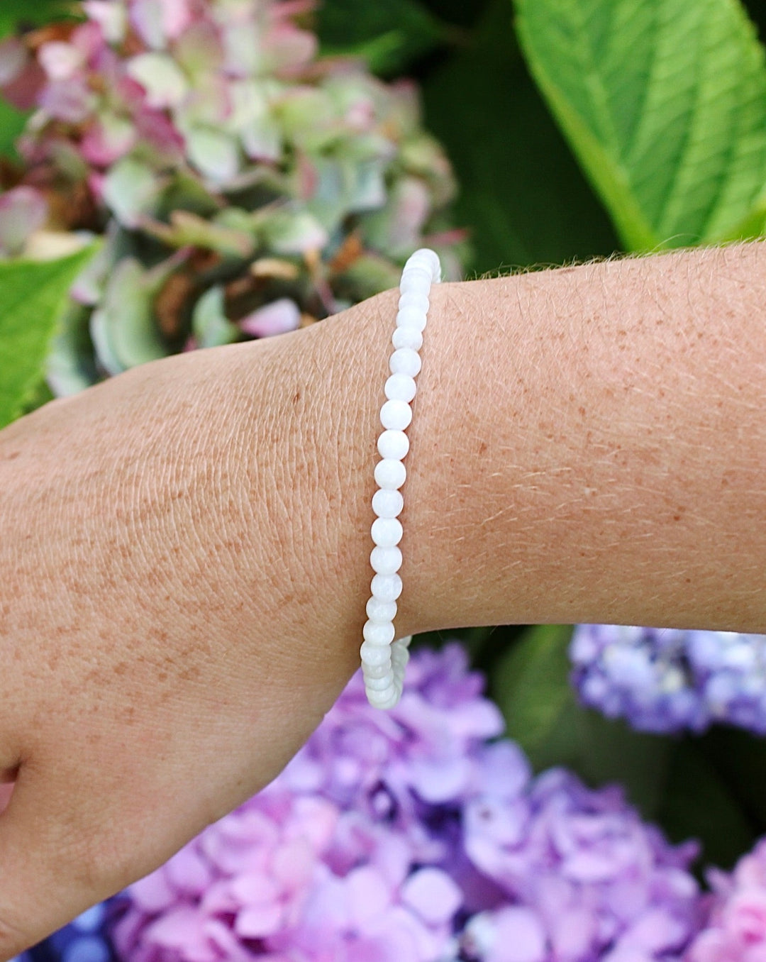 Moonstone 4mm Beaded Gemstone Bracelet on a wrist with flowers.