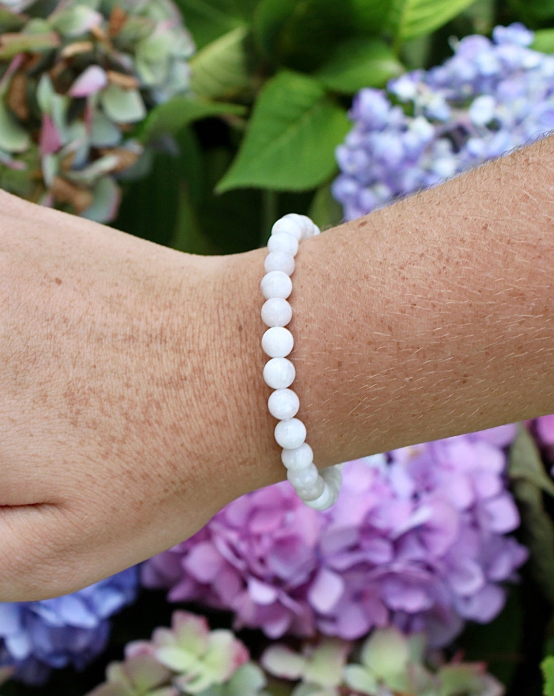 Moonstone 6mm Beaded Gemstone Bracelet on a wrist with flowers.