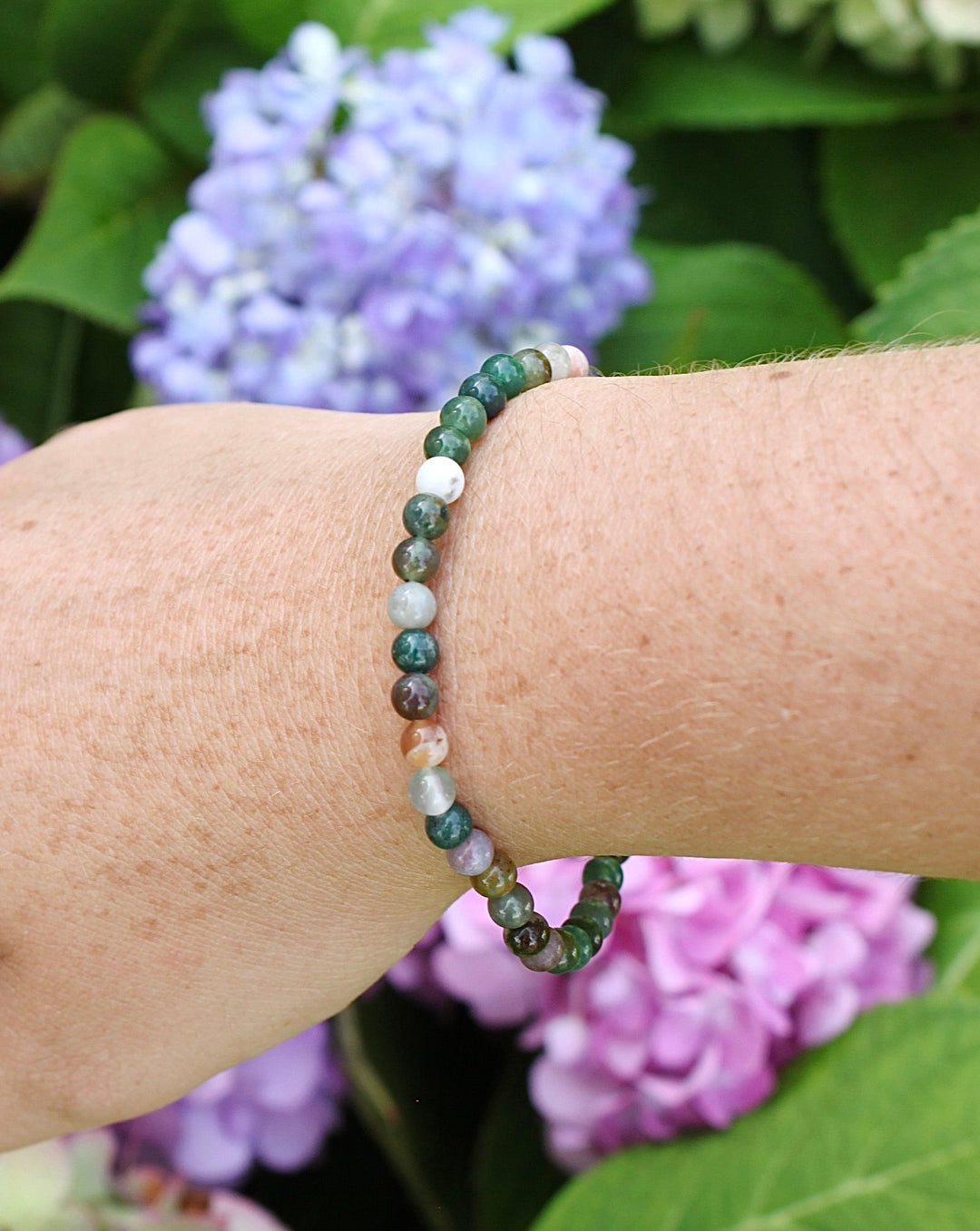 Moss Agate 4mm Beaded Gemstone Bracelet on a wrist with flowers.