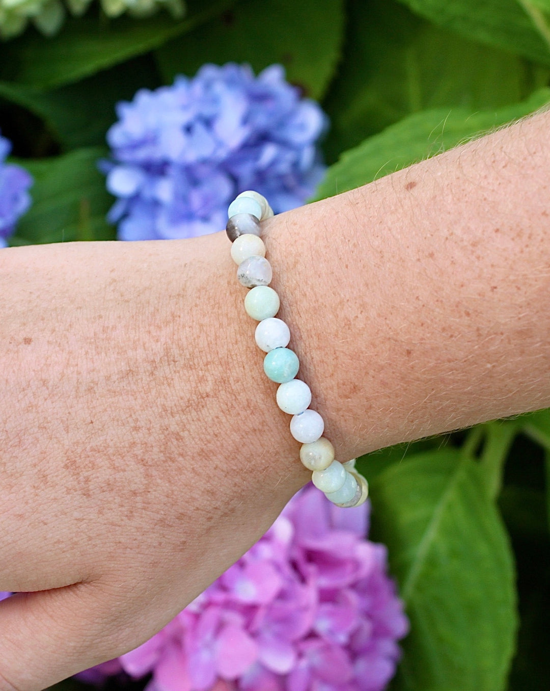 Multi Amazonite 6mm Beaded Gemstone Bracelet on a wrist with flowers.