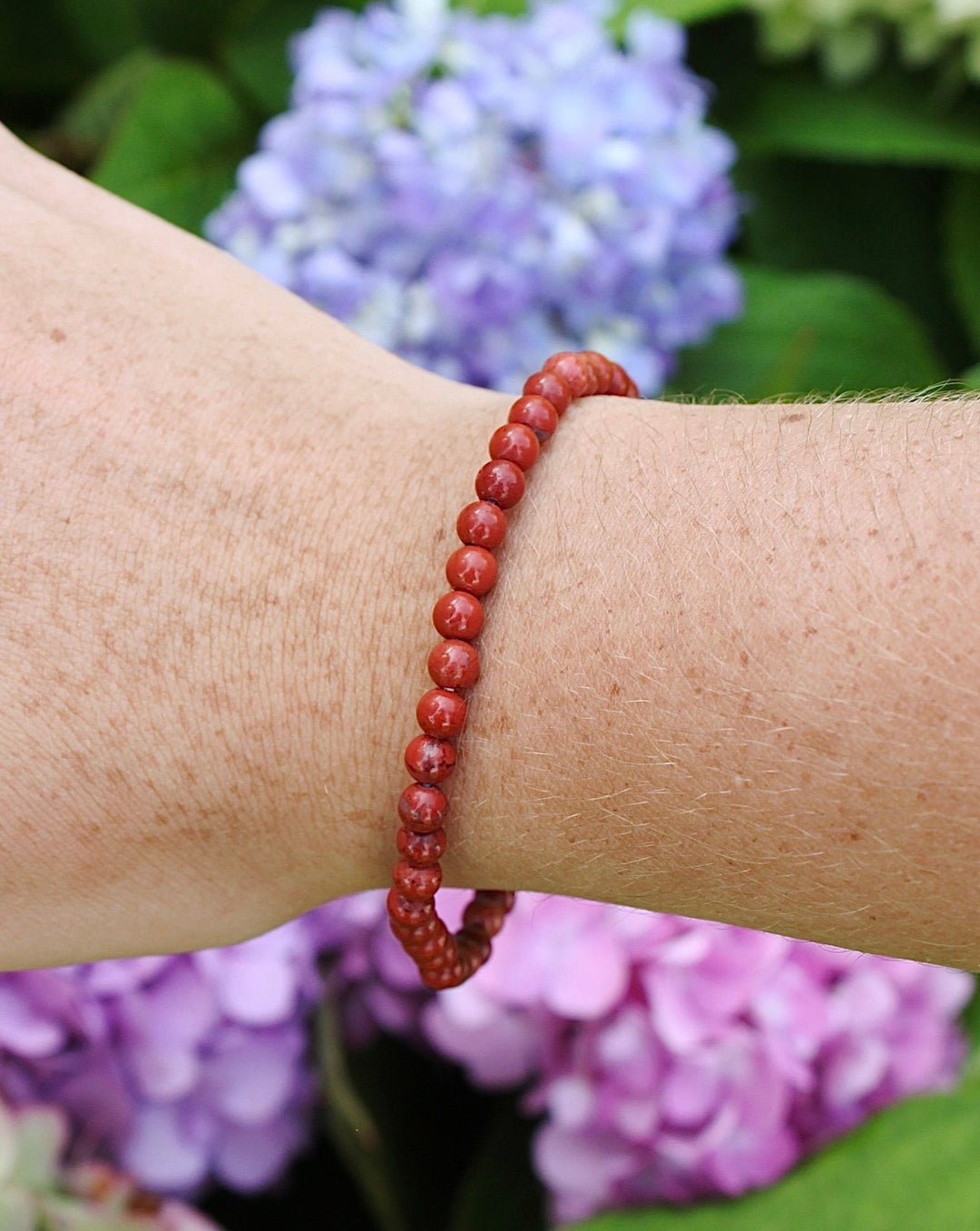 Red Jasper 4mm Beaded Gemstone Bracelet on a wrist with flowers.