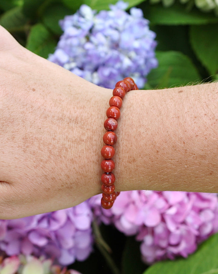 Red Jasper 6mm Beaded Gemstone Bracelet on a wrist with flowers.