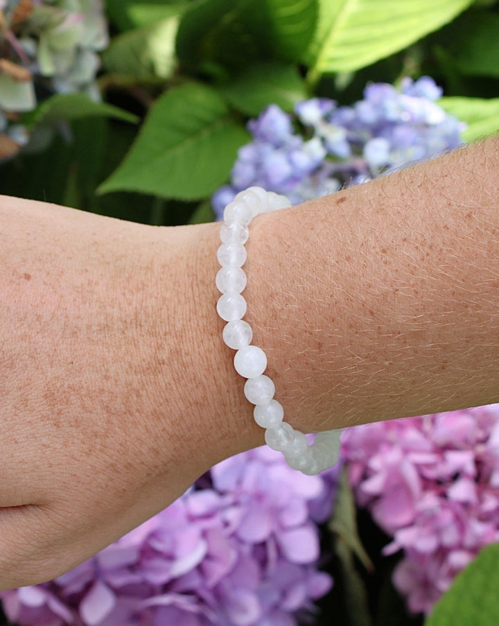 Snow Quartz 6mm Beaded Gemstone Bracelet on a wrist with flowers.