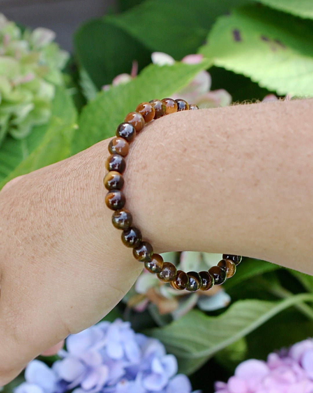 Tiger Eye 6mm Beaded Gemstone Bracelet on a wrist with flowers.