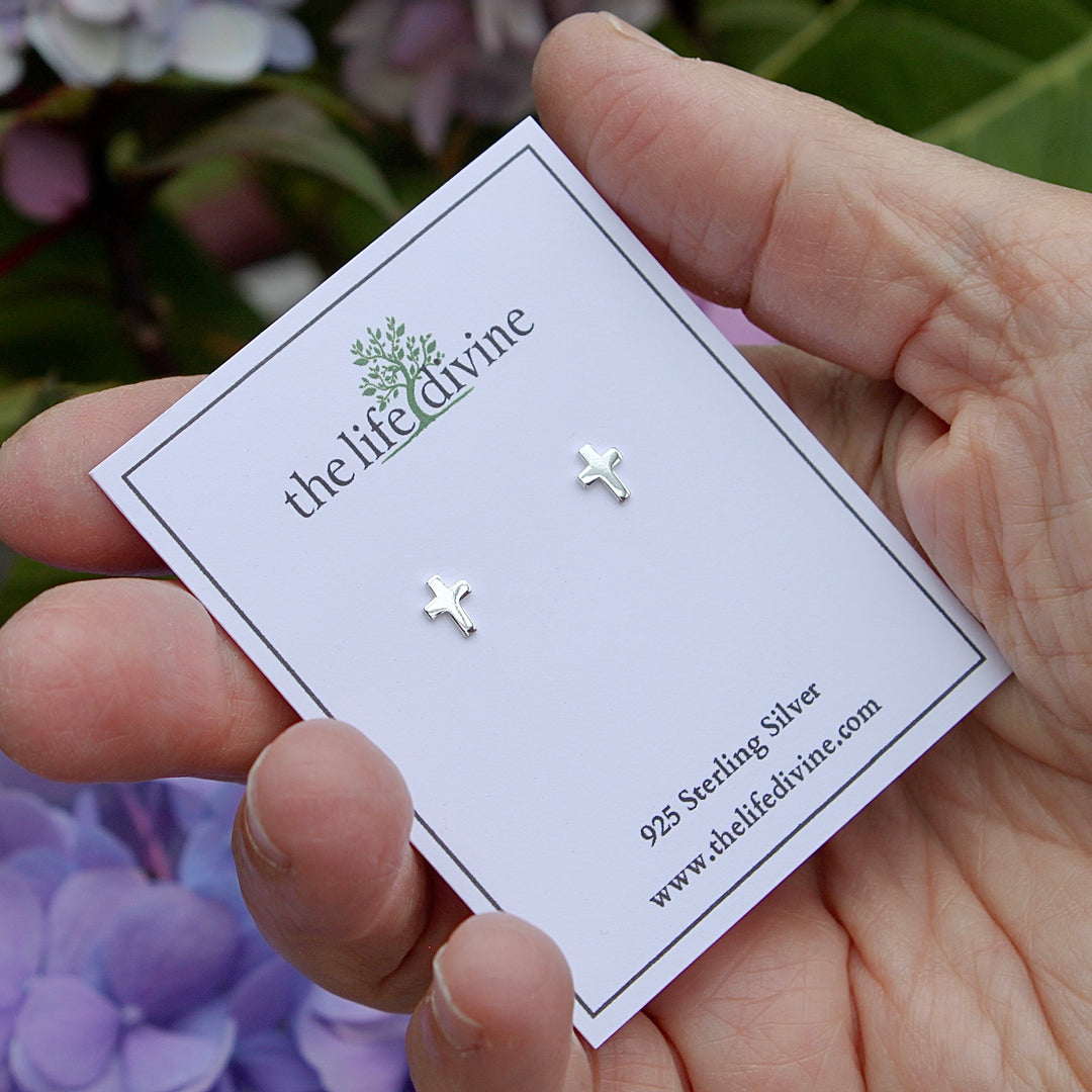 Tiny Cross Sterling Silver Earrings on a card held in a hand.