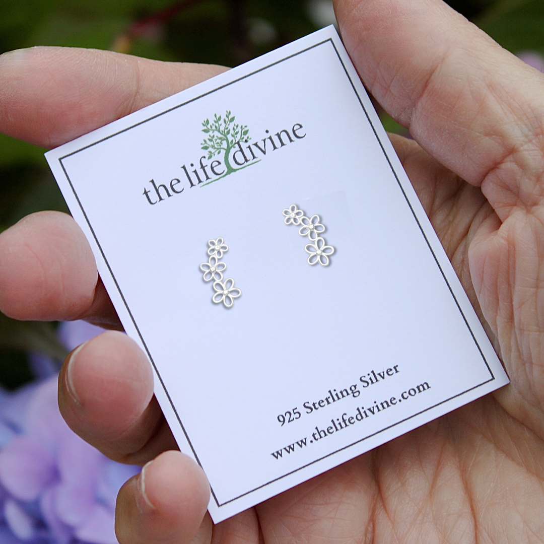 Trail of Three Flowers Earrings on a card held in a hand.