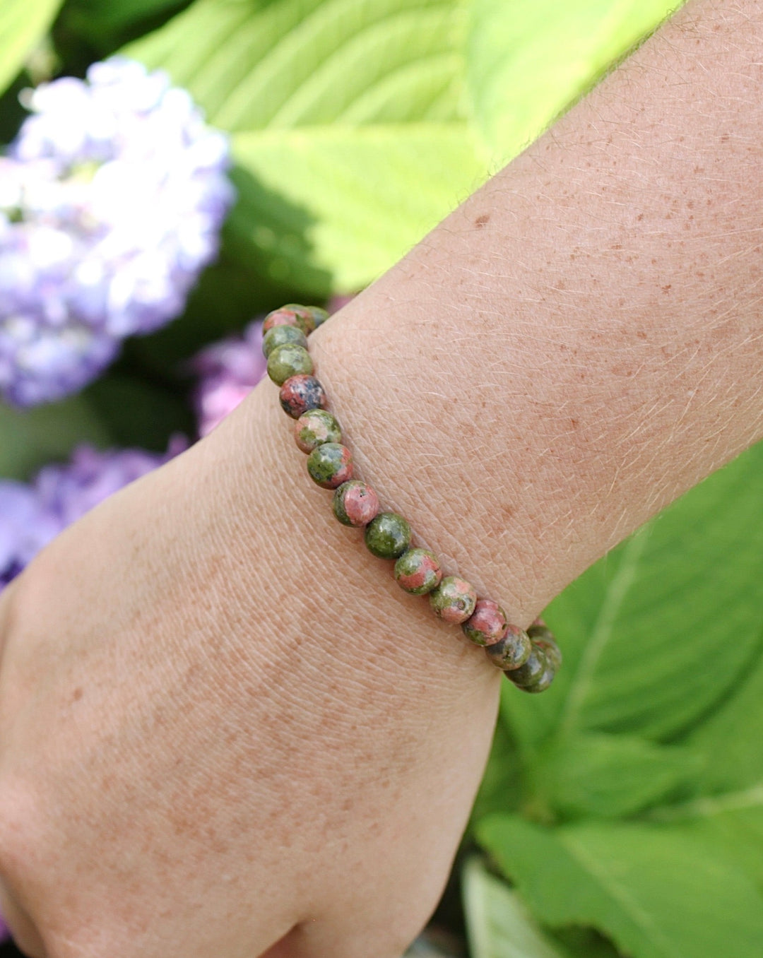 Unakite 6mm Beaded Gemstone Bracelet on a wrist with flowers.