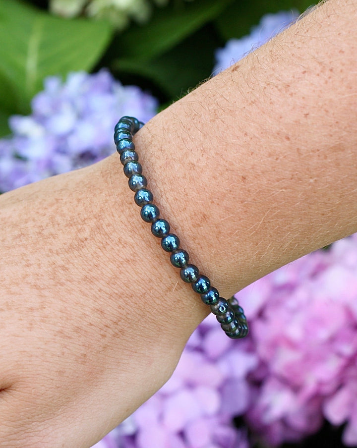 Aqua Aura 4mm Gemstone Bracelet on a wrist with flowers in background.