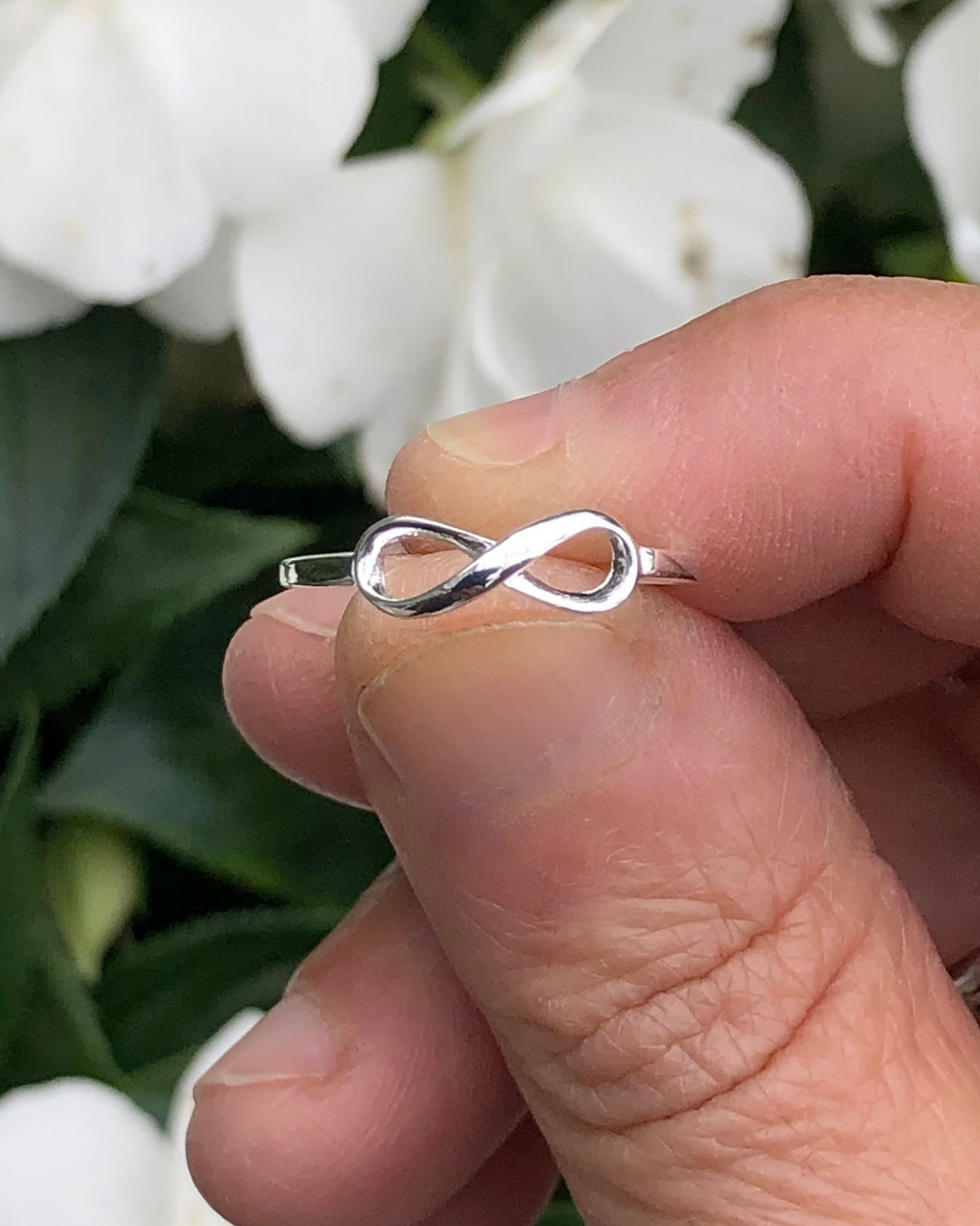 Silver Infinity Ring  between fingers with white flowers